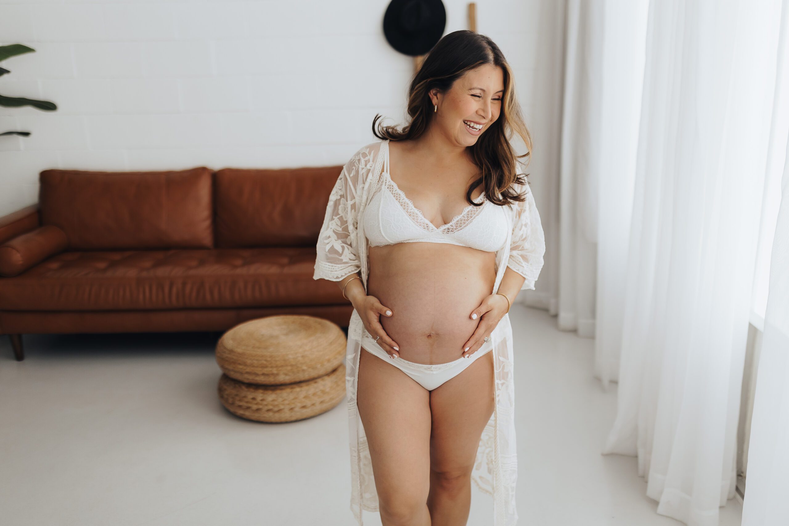 Pregnant woman stands in a beautiful studio holding her belly and laughing