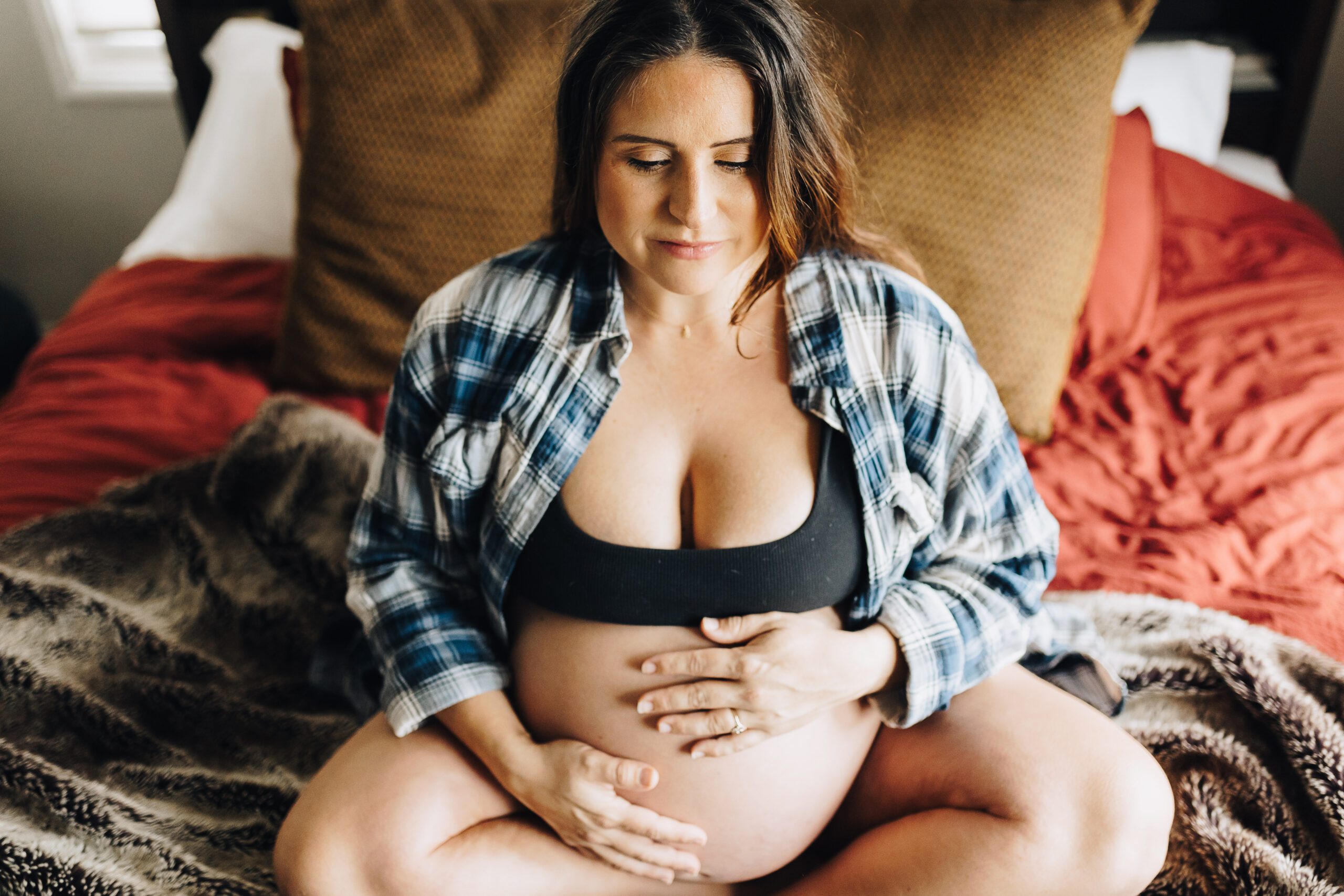 Pregnant mom sits on her bed showing her belly and breathing in the beauty of her pregnancy.