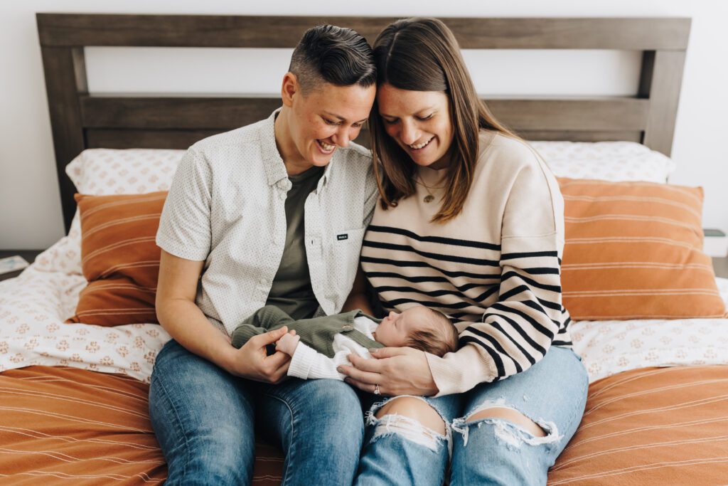 Two moms hold their newborn baby during an in-home photo session in Oakland, CA