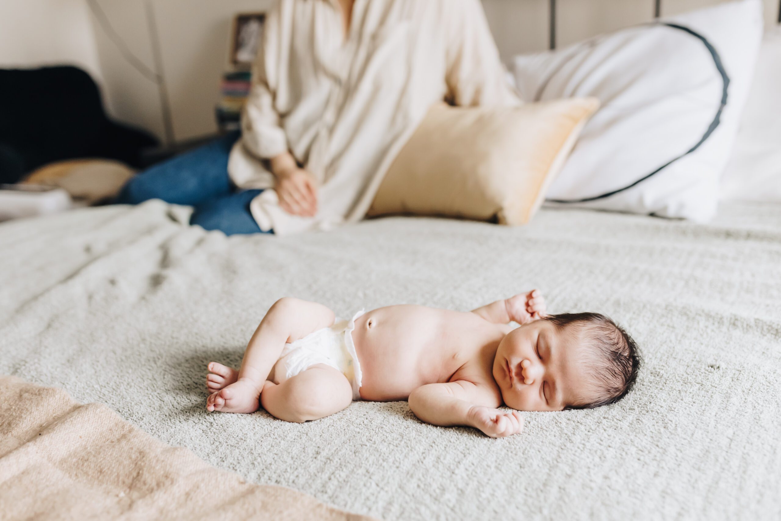 A newborn baby lays sleeping on the bed.