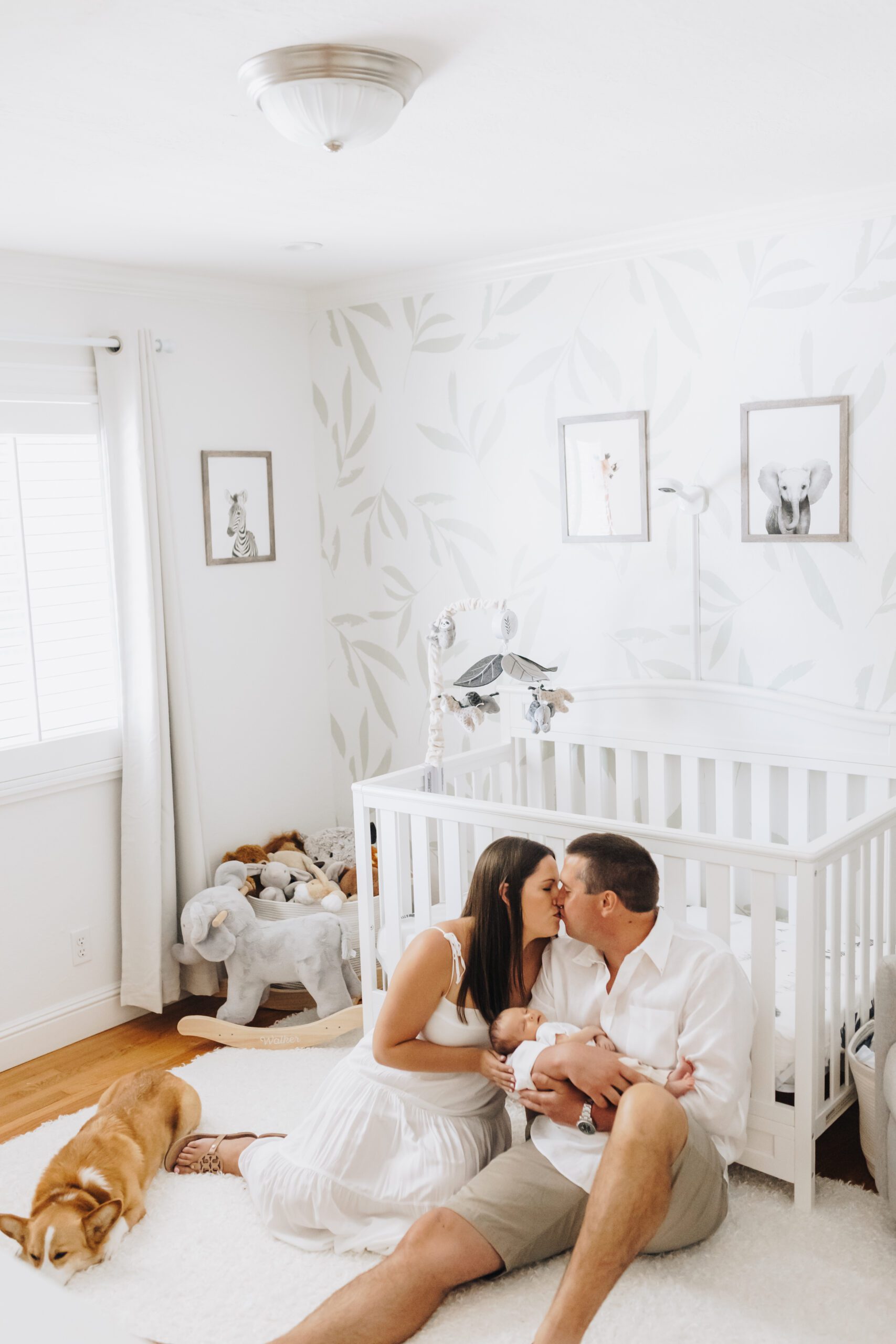 A couple holds their newborn baby in their nursery as their dog looks on.