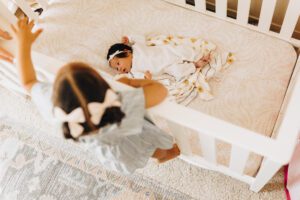 Big Sister watches over baby sister who is lying in the crib during an in-home lifestyle newborn session