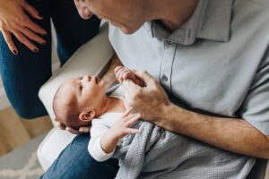 Dad holds baby and baby's hand is wrapped around dads finger