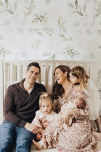 Family of five sits in front of crib holding new baby