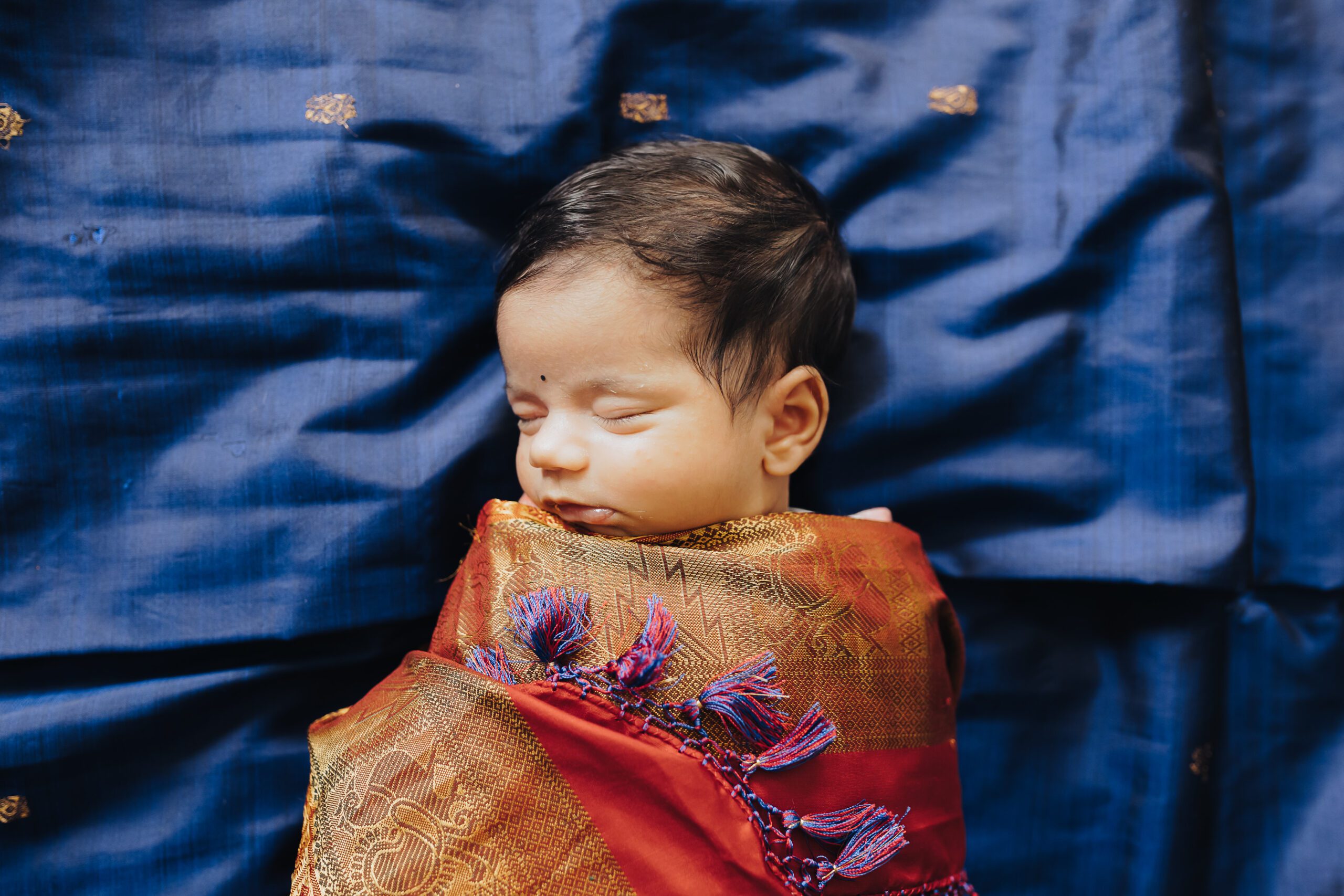 Baby wrapped in a sari lays on a bed sleeping during lifestyle newborn photography session