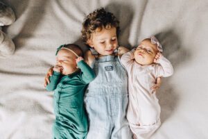 Big Brother lays on bed with twin baby sisters during newborn session