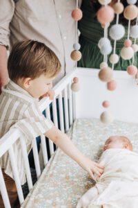 Toddler leans over crib to pat baby sister in Martinez newborn session