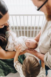 Overhead photo of sleeping baby swaddled, held by parents and big brother