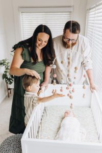 Toddler and parents look at baby sister in her crib in Martinez in-home session