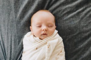 Overhead photo of Baby sister laying on the bed swaddled and asleep during lifestyle newborn session