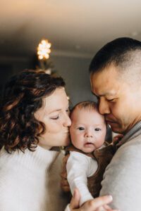 Parents kiss baby together during in-home session