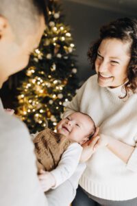 Mom and three month old baby smile at dad during in-home session