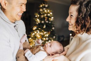 Mom and dad hold baby smiling with Christmas tree during in-home session