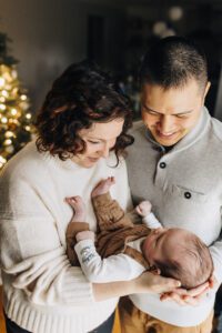 Parents hold baby who is looking up at them during an in-home three month session