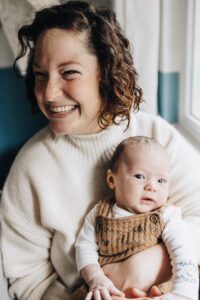 Mom smiles holding baby during in-home newborn session