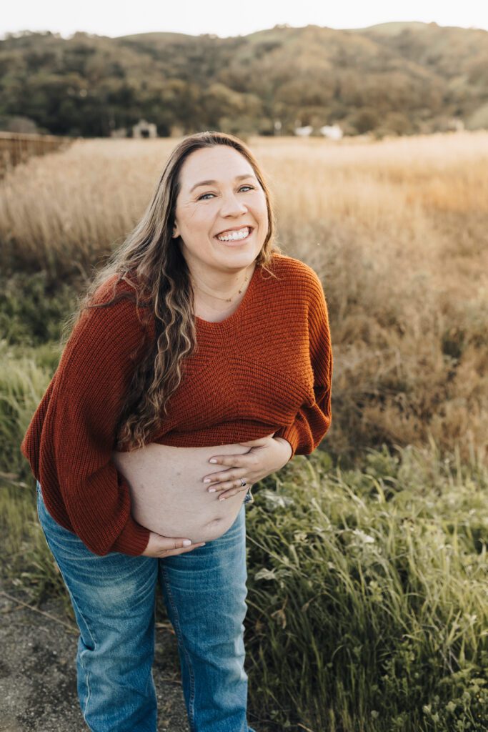 Pregnant woman shows her belly and laughs during a maternity session in Martinez, CA