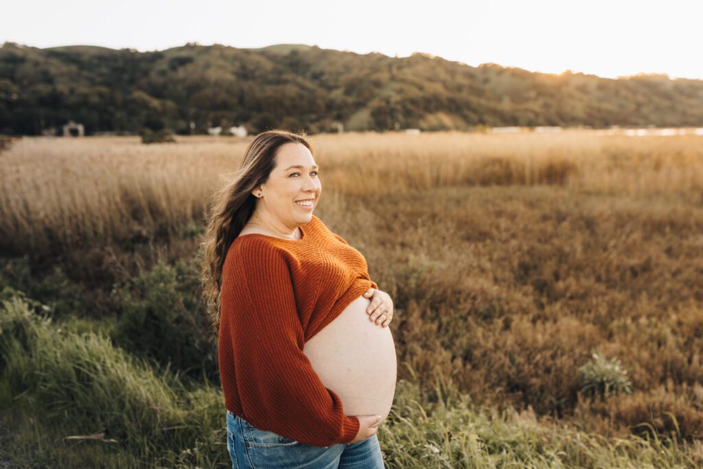 During a maternity session in Martinez, Ca a pregnant mom shows off her beautiful belly as the sun glows behind her. 
